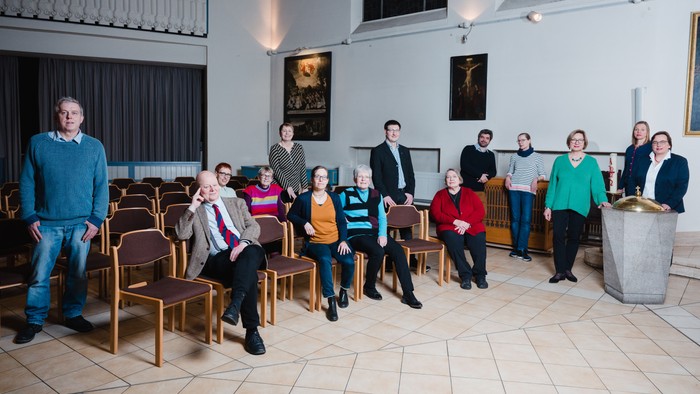 Eine Gruppe von Menschen posiert in einem Raum mit Stühlen und Bildern an den Wänden.