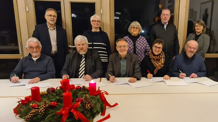 Gruppe von Personen, die um einen Tisch mit Festtagsdekoration sitzen und stehen.