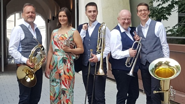 Fünf Personen halten Blasinstrumente aus Messing und posieren gemeinsam im Freien.