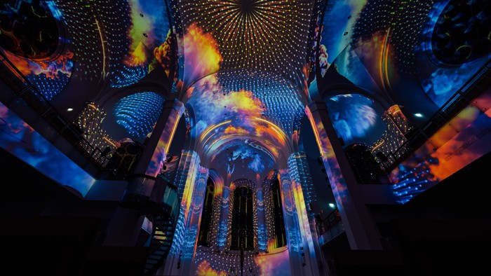 Lebendige, farbenfrohe Lichtprojektionen erzeugen einen faszinierenden, futuristischen Kuppel-Effekt in einem imposanten architektonischen Raum.