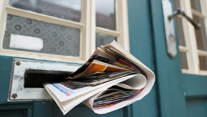 Überquellender Briefkasten an blauer Tür mit vielen Briefen und Werbung
