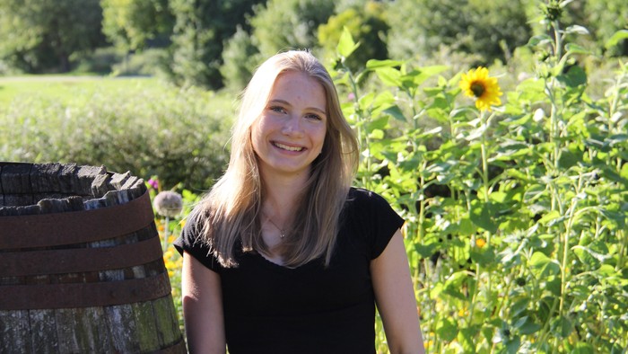 Kvinde i sort skjorte, der står ved træhegn og solblomster.