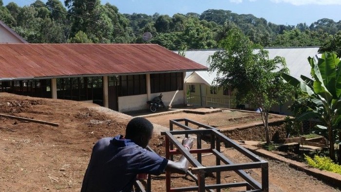 Vor dem Hintergrund eines Berges konstruiert ein Mann aus Tansania einen Rahmen aus Stahl