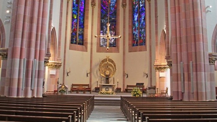 Innenraum einer Kirche mit hohen Säulen, Kirchenbänken und bunten Glasfenstern