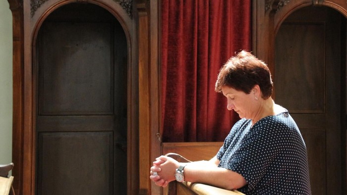 Frau kniet in einer Kirchenbank, die Hände zum Gebet gefaltet.