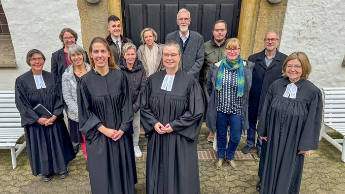 Eine junge Pfarrerin mit drei Kolleginnen im Talar sowie einer gemischten Menschengruppe vor einer Kirchentür