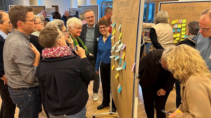 Gruppe von Menschen, die sich um ein Board mit Haftnotizen versammelt.