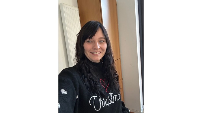 Eine Frau mit einem schwarzen Shirt, auf dem „Christmas“ steht, lächelt.