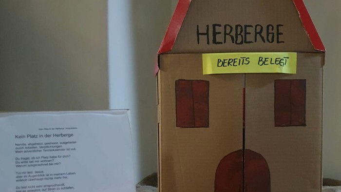 Pappkartonhaus mit Schild „Herberge“ und Notiz auf dem Tisch