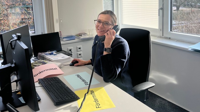 Olivia sitzt am Schreibtisch mit Fördermittelinformationen