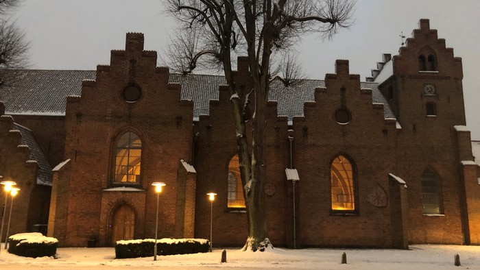 Gamle teglsteinskirke med snø på jorden og lyse lygter.