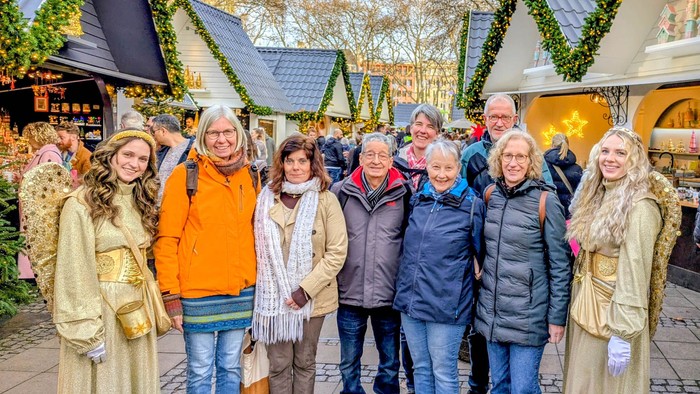 Eine gemischte Gruppe, flankiert von zwei als Engel verkleideten jungen Frauen, auf einem Weihnachtsmarkt