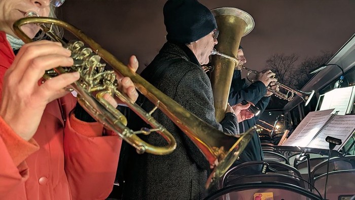 Trompeterin und andere Blasmusiker:innen spielen abends im offnen Cabriobus
