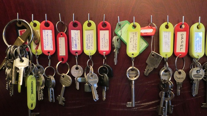 Viele Schlüssel an unterschiedlich farbigen Schlüsselanhänger und Beschriftungen hängen an einem Schlüsselbrett