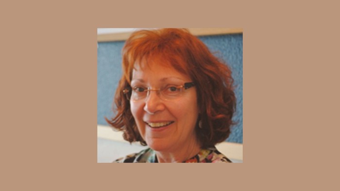 Eine Frau mit rotem Haar und Brille lächelt in die Kamera.