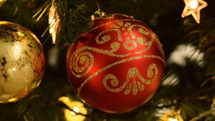 Ein roter Weihnachtschmuck mit goldener Glitzerverzierung hängt am Baum.