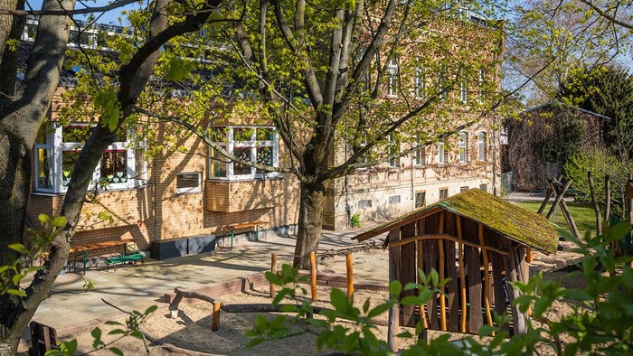Ein ruhiger Innenhof mit Holzbänken, einer kleinen Hütte und umgeben von Bäumen und Gebäuden.