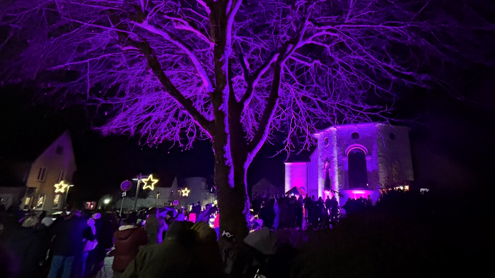 Nachtveranstaltung mit Menschenmenge, beleuchtetem Baum und erleuchtetem Torbogen