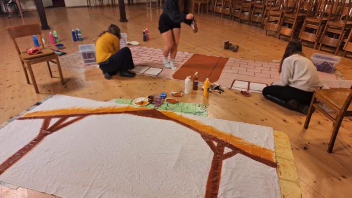 Menschen, die in einem Raum mit Holztischen und -stühlen an Kunstprojekten arbeiten.