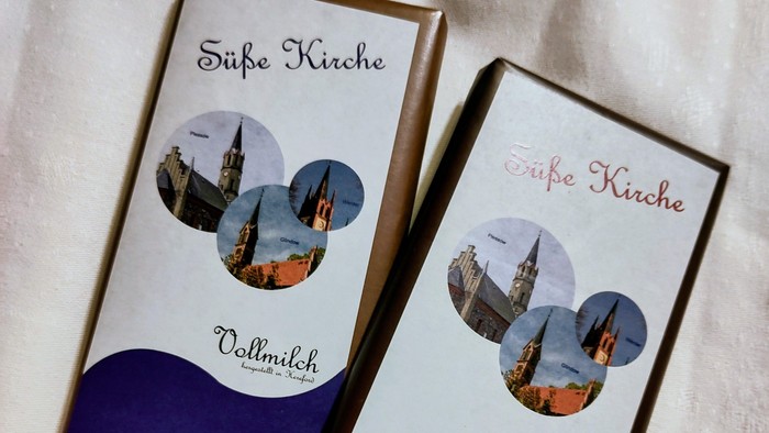 Zwei Schokoladenriegel mit der Aufschrift „Süße Kirche“ und Abbildungen von Kirchtürmen auf der Verpackung.