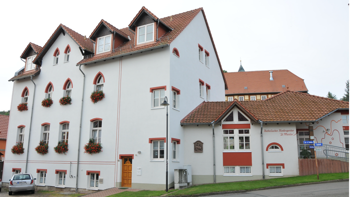 Das Bild zeigt ein weißes Gebäude mit roten Akzenten und Blumenkästen an den Fenstern.