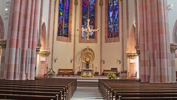 Innenraum einer Kirche mit hohen Säulen, Kirchenbänken und bunten Glasfenstern