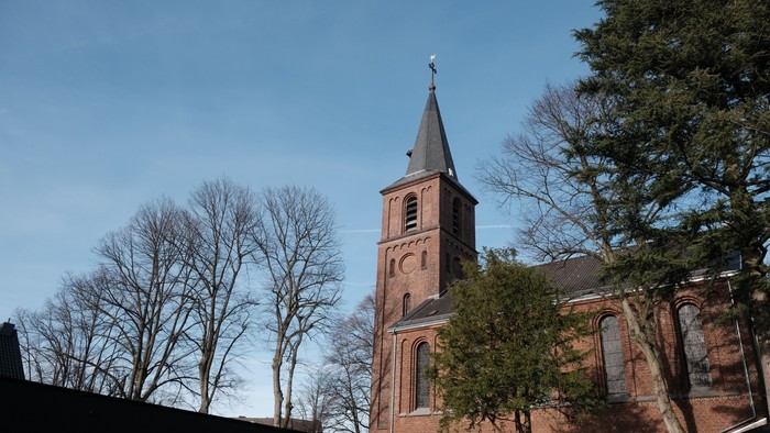 Kirchturm aus rotem Backstein vor klarem Himmel und Bäumen