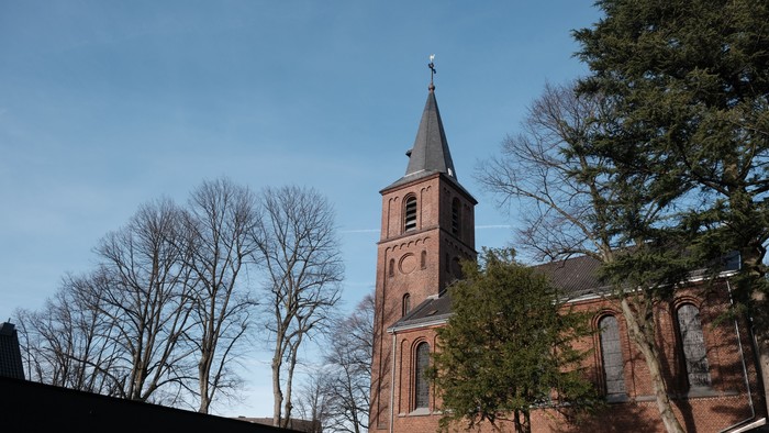 Kirchturm aus rotem Backstein vor klarem Himmel und Bäumen