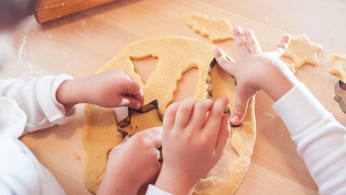 Kinder, die Plätzchenteig mit Ausstechformen ausstechen.