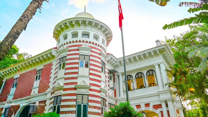 Historisk bygning med røde og hvide striber, toppet med et flag, omgivet af grønt