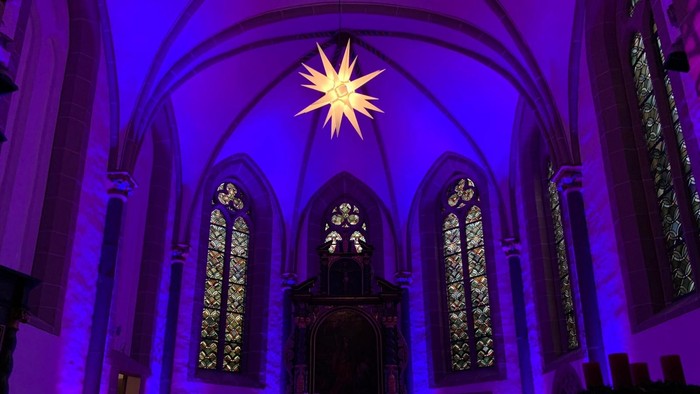 Kirchlicher Innenraum mit violettem Licht und Sternenprojektion.