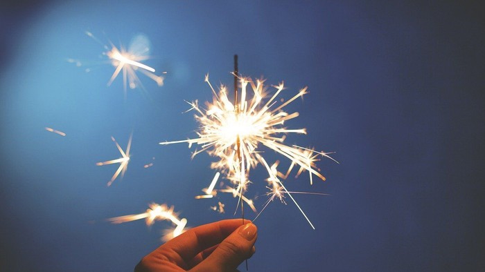Eine Hand hält ein brennendes Feuerwerk vor dunklem Himmel
