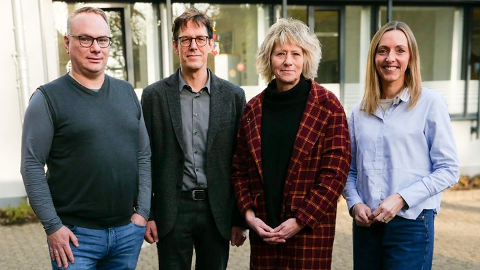 Zwei Männer und zwei Frauen stehen vor einem Bürogebäude und lächeln in die Kamera