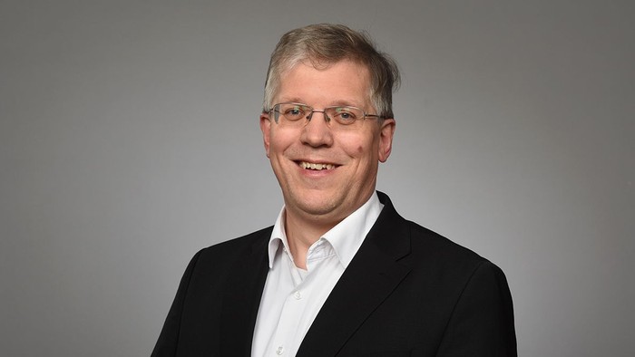 Mittelalter Mann mit Brille, der einen schwarzen Blazer und ein weißes Hemd trägt.