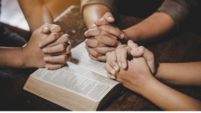 Hände über einem offenen Buch gefaltet, was Gebet oder Einheit andeutet.