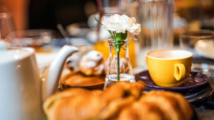 Frühstückstisch mit Pfannkuchen, Kaffee und Blumen.