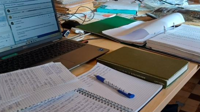 Überfüllter Arbeitsplatz mit Laptop, Notizbüchern, Papieren und Büroartikeln auf einem Schreibtisch.