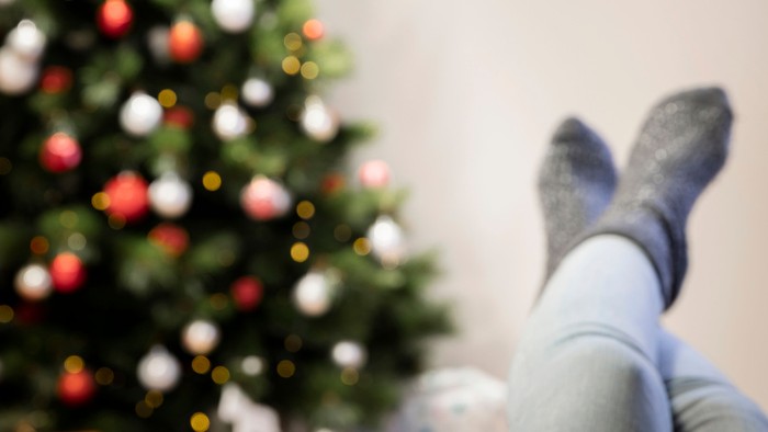 Eine Frau hat die Beine hochgelegt, eine volle Kaffeetasse in der Hand und schaut auf einen Weihnachtsbaum