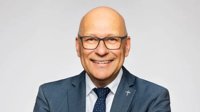 Ein Mann mit Brille und Anzug lächelt in die Kamera.