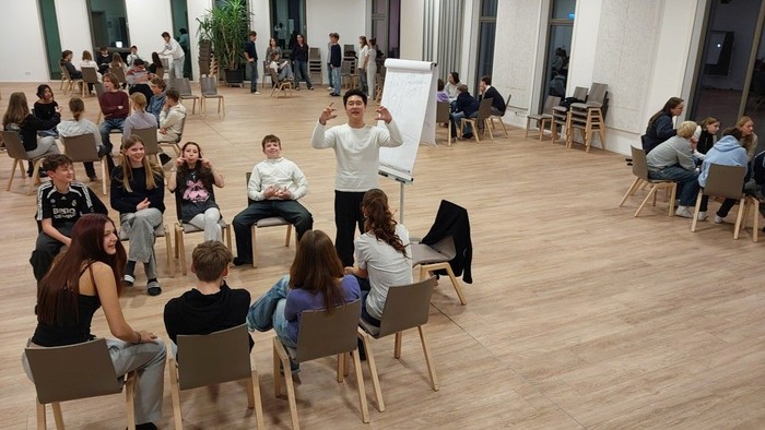 Juugendliche in einem Raum haben Spass bei einem Spiel bei dem etwas auf ein Flip-Chart geschrieben wrid.