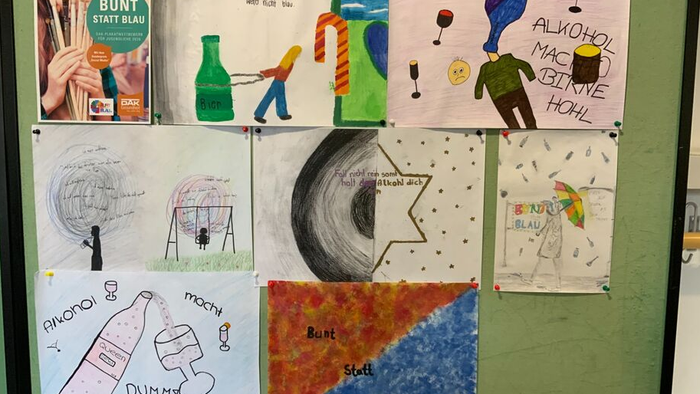 Kinderkunstwerke und Plakate zum Thema Alkoholaufklärung, darunter humorvolle und lehrreiche Motive auf einer Pinnwand.