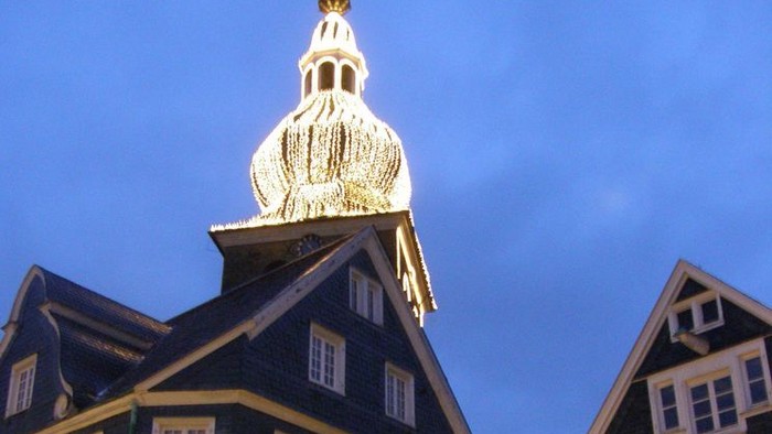 Ein weißer Turm mit goldener Kuppel ragt über schwarze Gebäude mit weißen Fenstern.