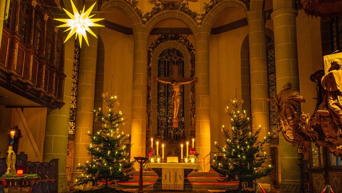 Elegante Kircheninnenausstattung, geschmückt mit Weihnachtsbäumen, goldenen Lichtern und einer Kreuzigungsszene während der Festtagszeit.