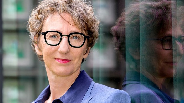 Julia Helmke vor einer sie reflektierenden Glaswand.