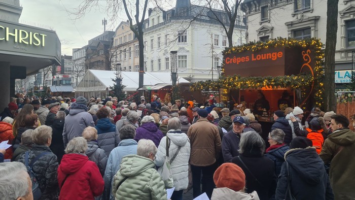 Überfüllter Freiluftmarkt mit festlichen Dekorationen und einem „Crêpes Lounge“-Stand im Winter.