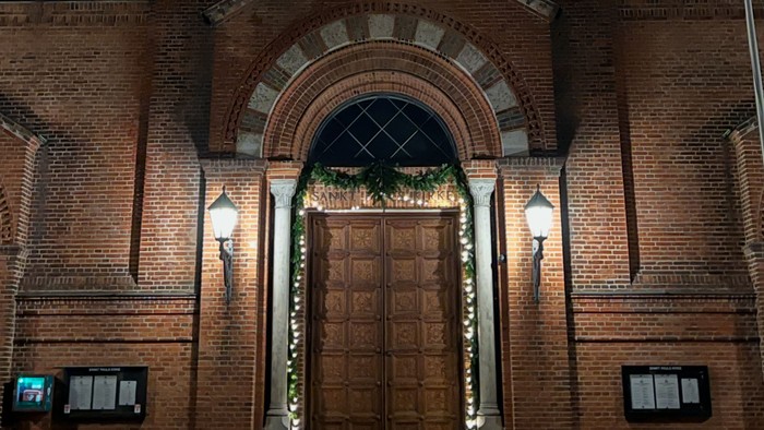 Elegant murstenskirkefacade pyntet med festlige lys og en stor buet indgang om natten.