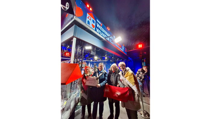 Die Gruppe feiert nachts in der Nähe eines geschmückten Busses mit roten Fahnen und winterlichen Lichtern.