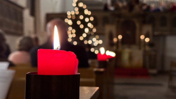Ein Gottesdienst zu Weihnachten in einer traditionellen Kirche. Im Vordergrund eine rote Kerze. Verschwommen im Hintergrund ein Weihnachtsbaum im Altarraum.
