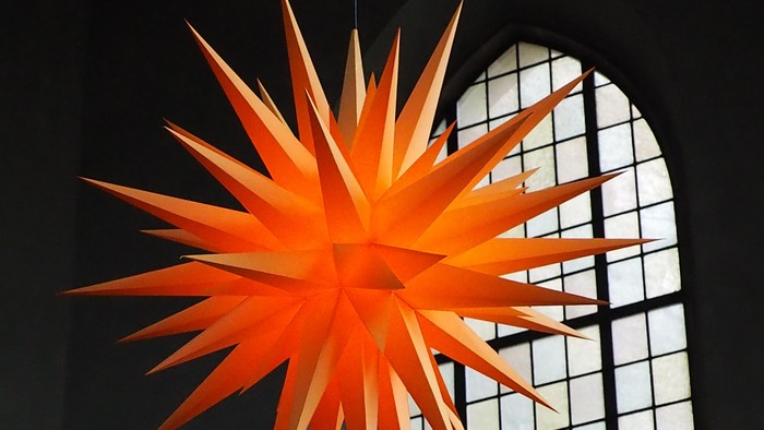 Helle orangefarbene Stern-Dekoration, die nahe einem großen Fenster hängt.