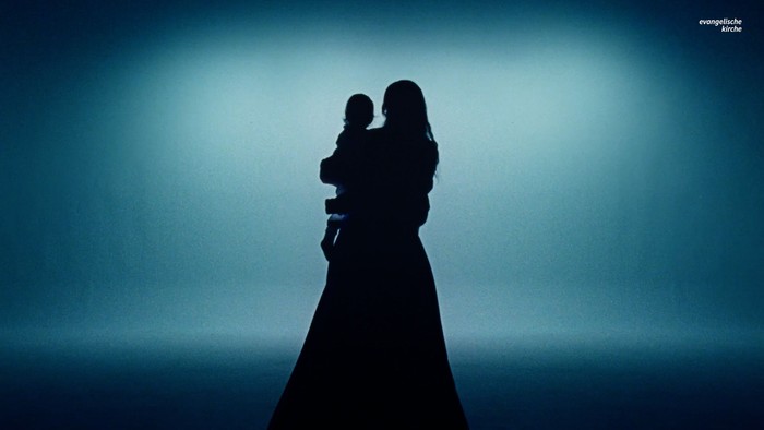 Silhouette einer Frau, die ein Kind vor einem stimmungsvollen, gradienten Himmelshintergrund hält.